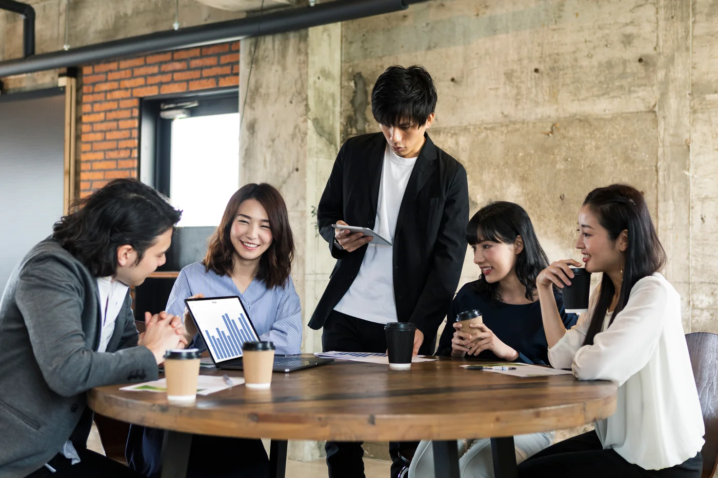 ノートパソコンとタブレットを囲んで打ち合わせする5人